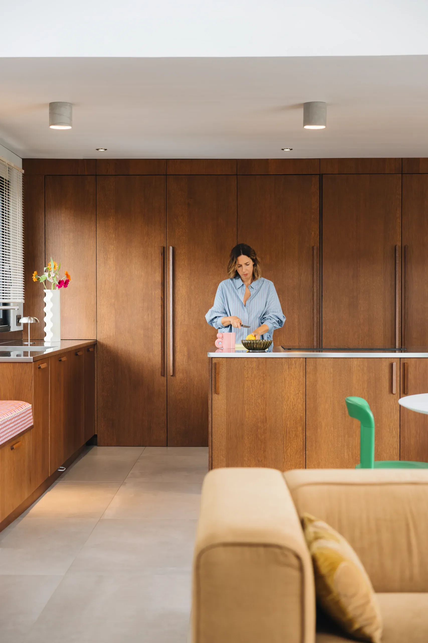 Cuisine teinte noyer — vue depuis le canapé, plan inox brossé et linéaire de façades chaleureuses