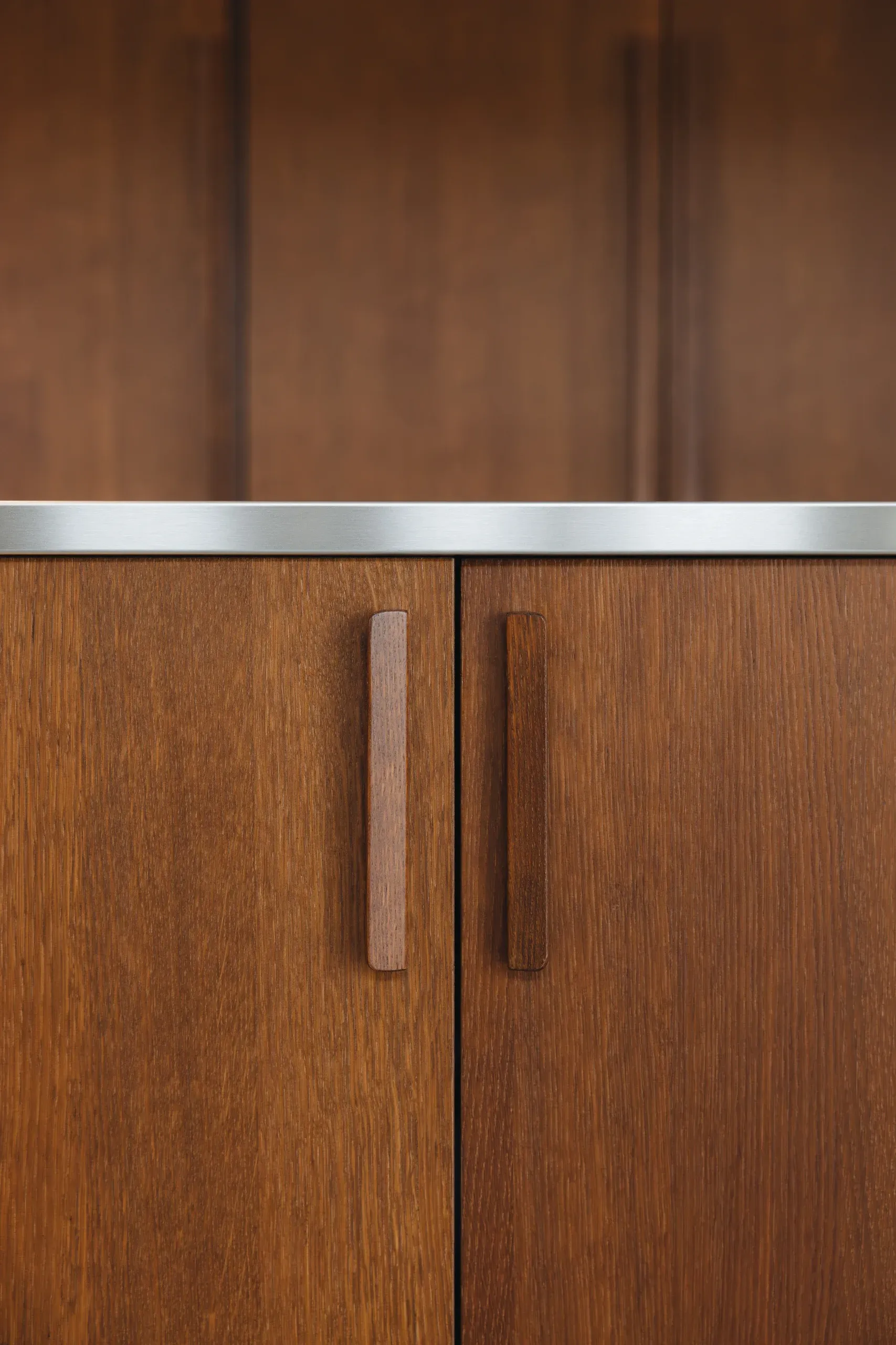 Détail des poignées bois massif sur façade chaude — jonction avec le plan inox brossé