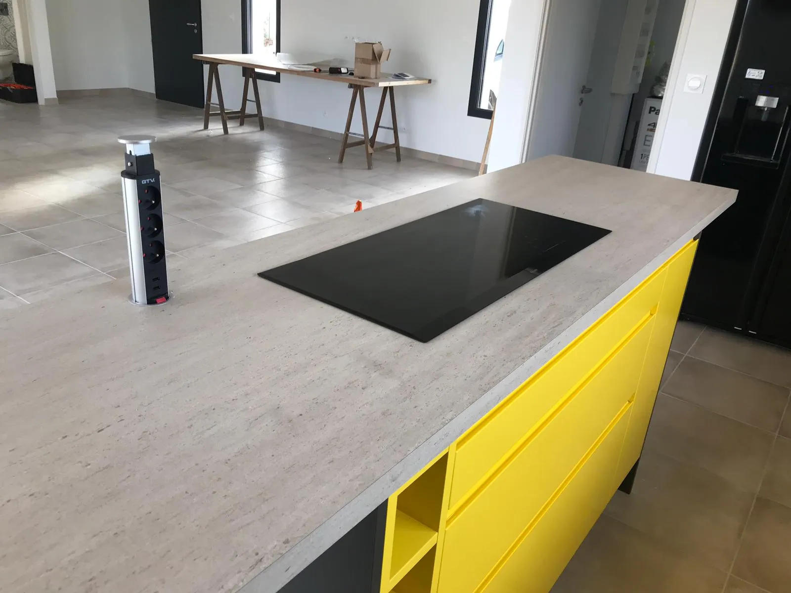 Cuisine jaune — détail du plan de travail béton avec plaque à induction et prise escamotable